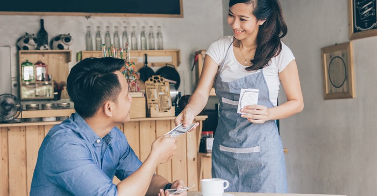 Man in coffee shop paying waitress with currency