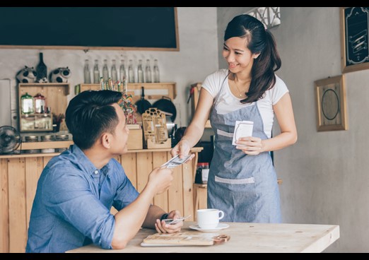 Man in coffee shop paying waitress with currency