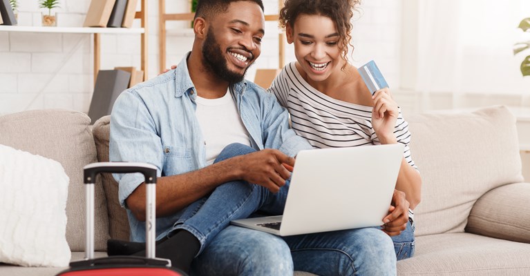 Couple with suitcase and laptop paying for something on credit card