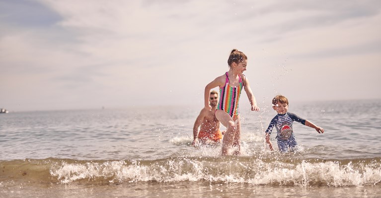 Children running through the sea with their dad behind them