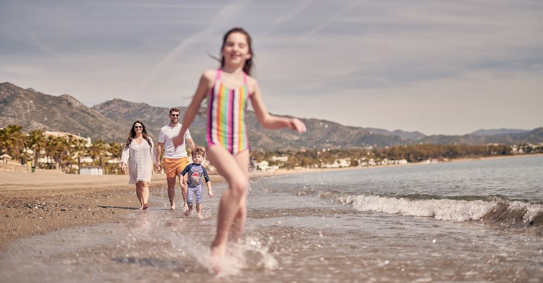 Young girl walking through the sea with family behind her