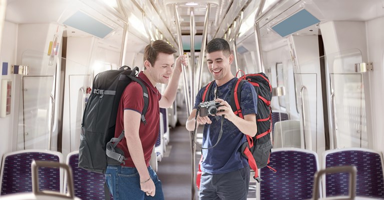 Two young males on a train with luggage looking at a camera