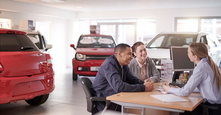 Couple smiling at saleswoman in car showroom