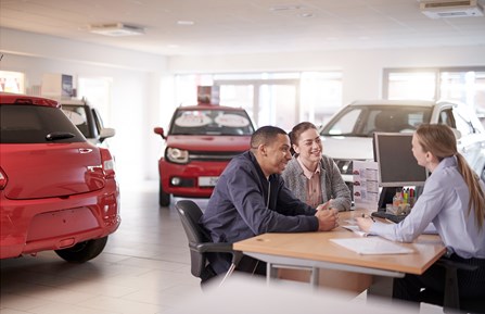 Couple smiling at saleswoman in car showroom