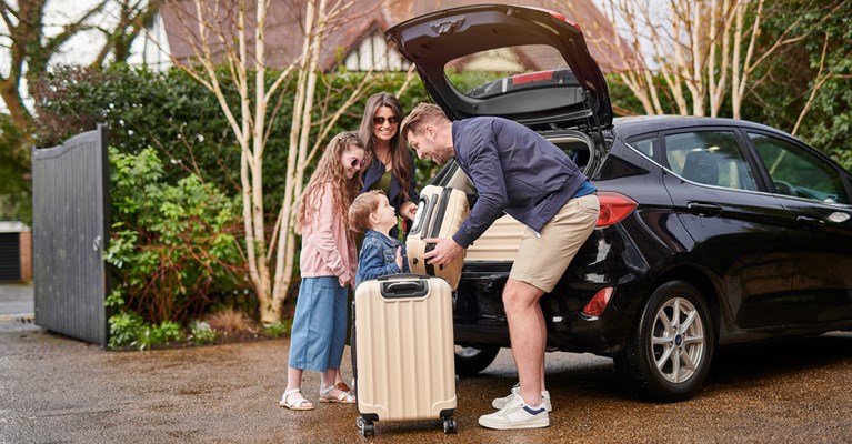 Family lifting suitcase into back of black car going on holiday