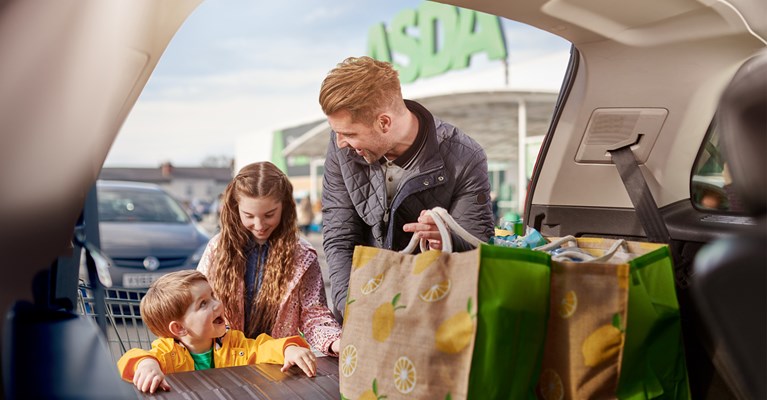 Dad and young children loading shopping into boot of car at Asda