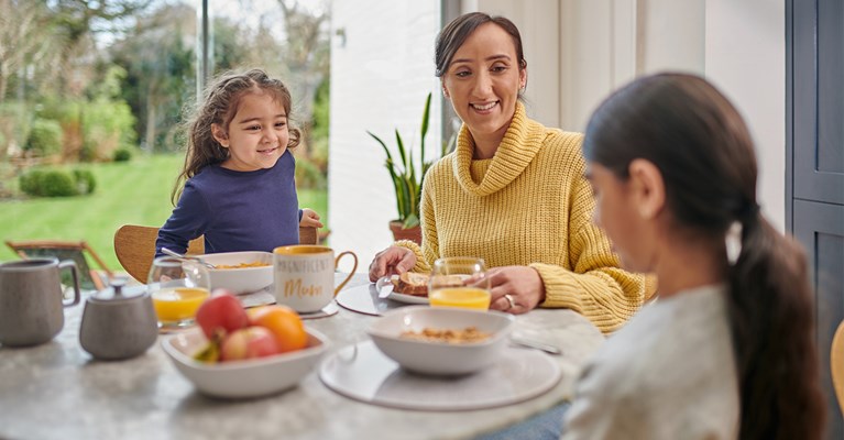 Mum and two daughter sat around table eating breakfast