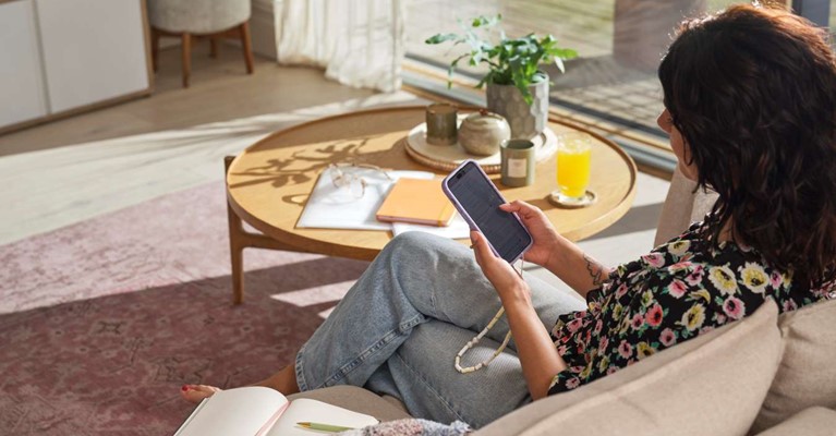 A woman sits on a sofa and uses her phone