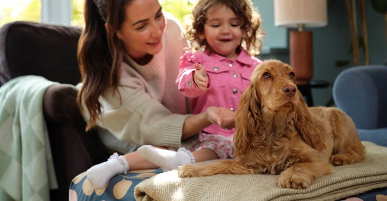 Puppy sits on a blanket while a woman and her daughter look on