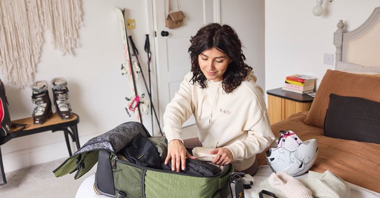 A woman packs a suitcase with skiing equipment