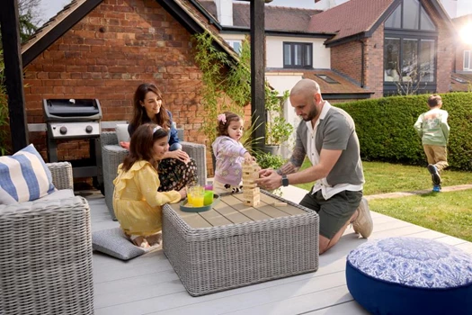 A family sit on the decking in their garden and play board games