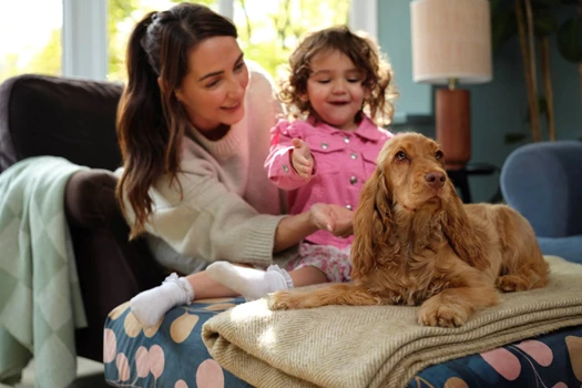 A mother and young daughter look at a puppy sat on a rug