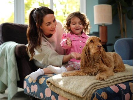 A mother and young daughter look at a puppy sat on a rug