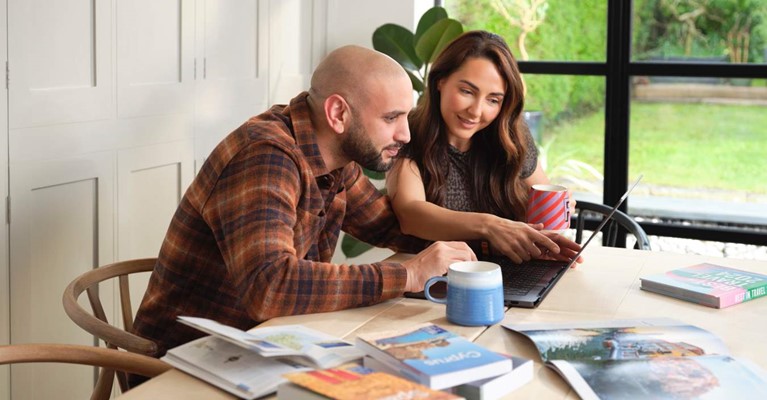 A couple sit at a table and look at a laptop