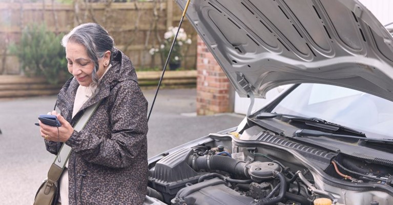 A woman uses a phone next to her broken down car