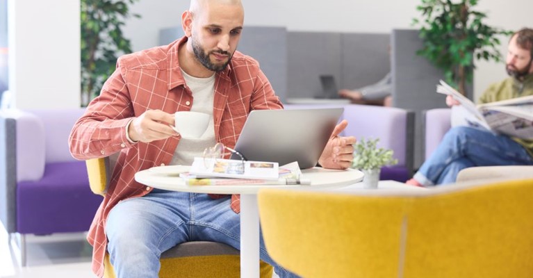 A man looks at a laptop while holding a drink