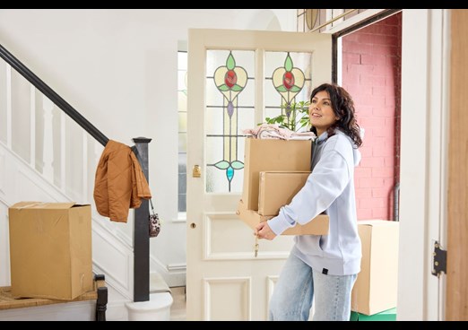 A woman walks into her new home holding boxes