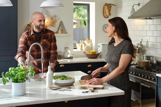 A young couple stand at a kitchen counter and talk