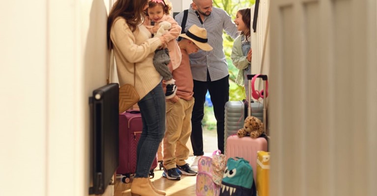 A family stand in a hallway with their luggage