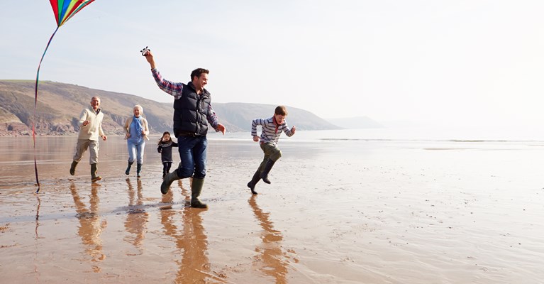 Family and grandparents playing on the beach with a kite