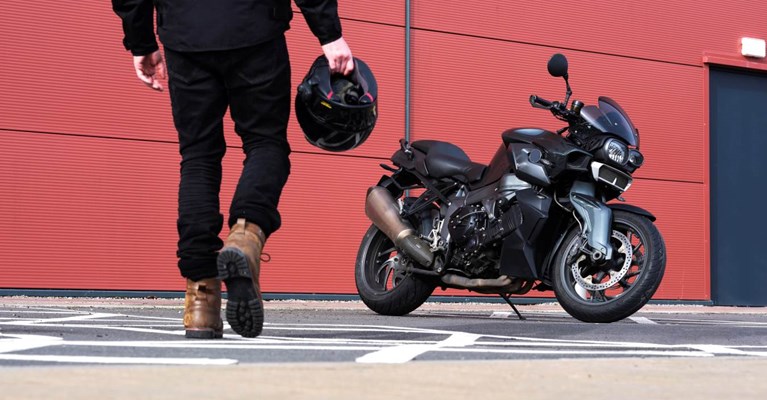A motorcyclist walks towards his motorbike holding a helmet