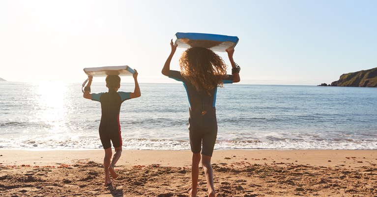 Young children running into the sea with body boards