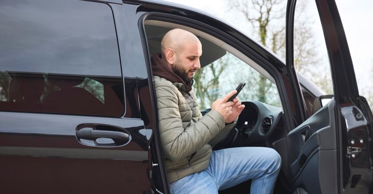 A man exits a van looking as his phone