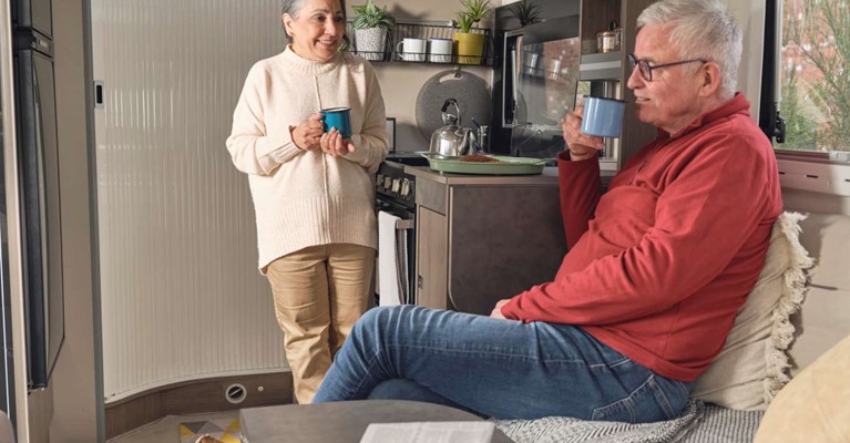 A man and woman have a drink in a caravan and talk