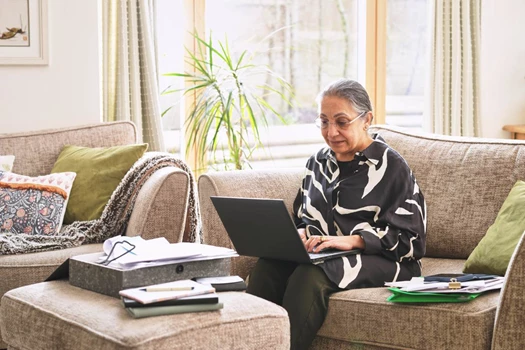 A woman sits on a sofa and looks at a laptop