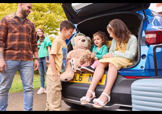 Children sit in the open boot of a car with teddy bear