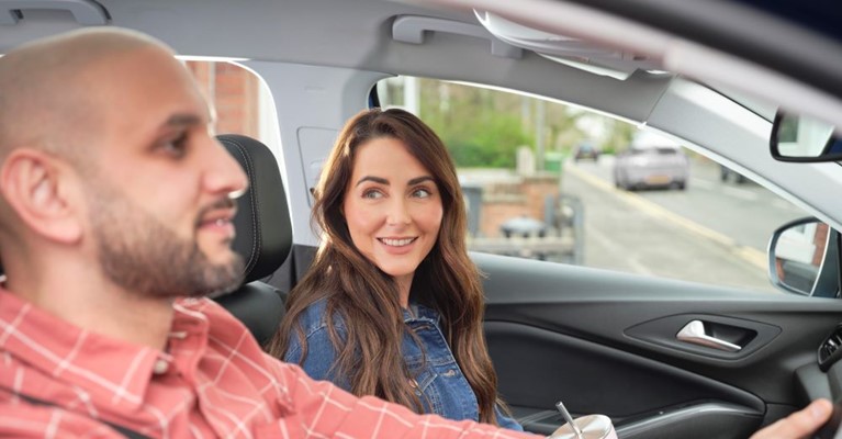 A woman looks towards a man as he drives a car